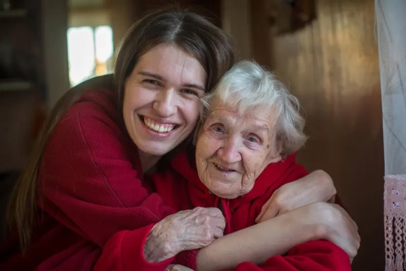 Adult daughter embracing elderly mother in a warm home