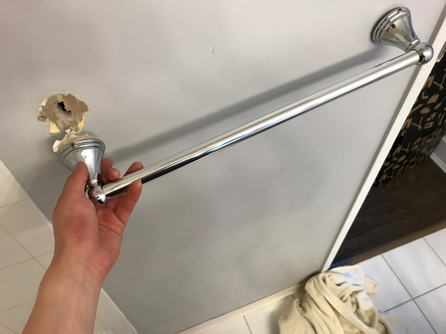 Towel bar ripped from bathroom tile wall — exposed drywall