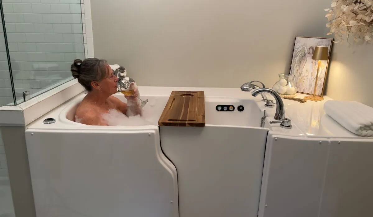 Woman relaxing in a walk-in tub with a bath tray and glass of wine